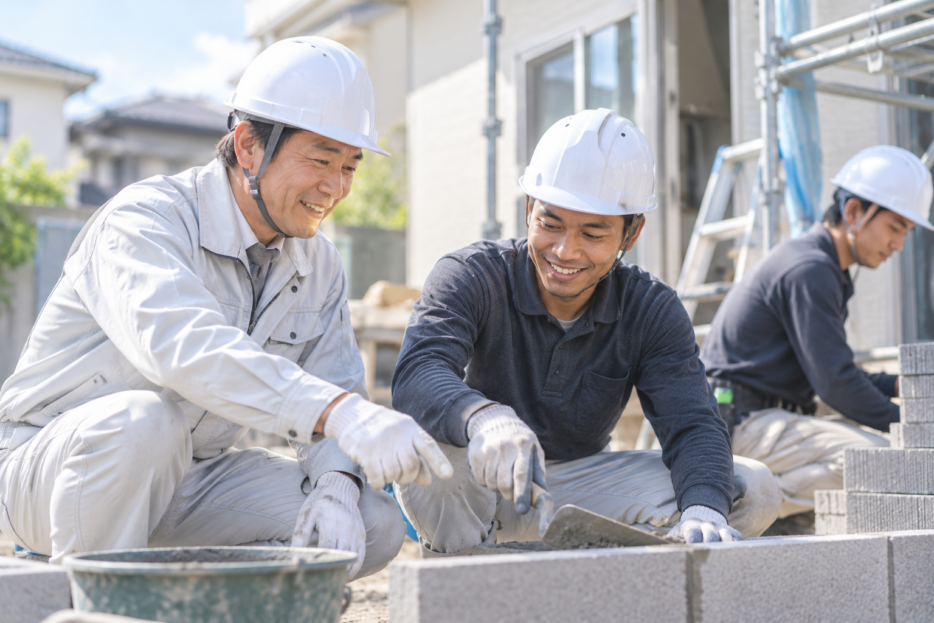 建設現場でベテランの日本人技能者と外国人技能者がブロック積みをしている様子